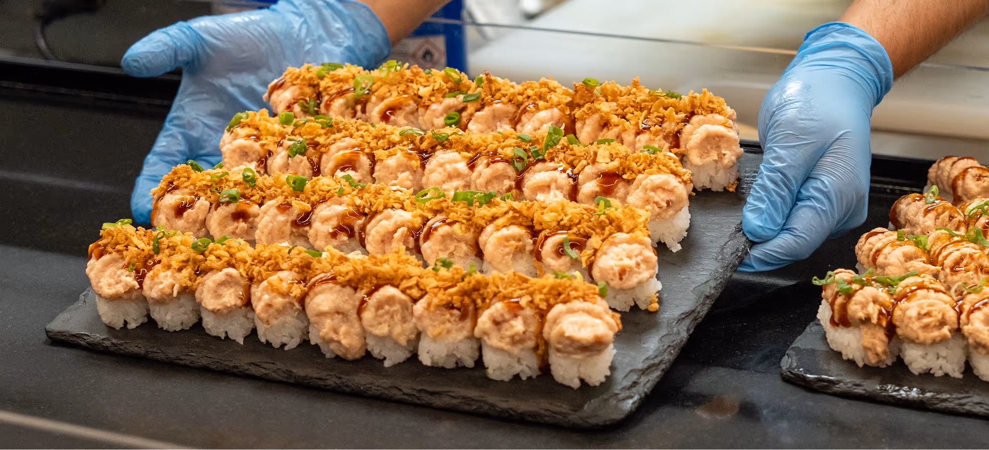 Tray of sushi rolls topped with sauce and crispy flakes.