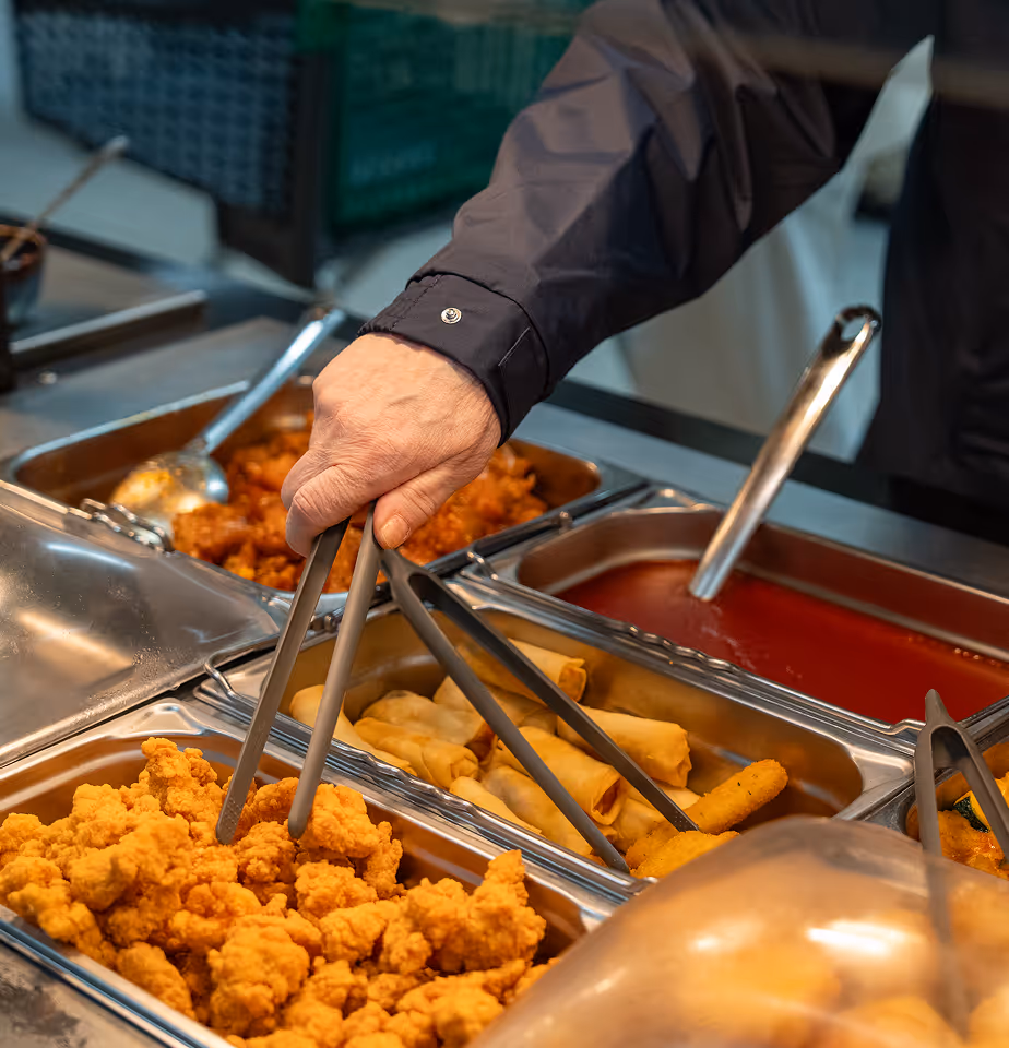 Person using tongs to serve fried chicken from buffet trays.