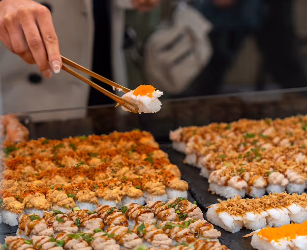 Person picking sushi from display using chopsticks.