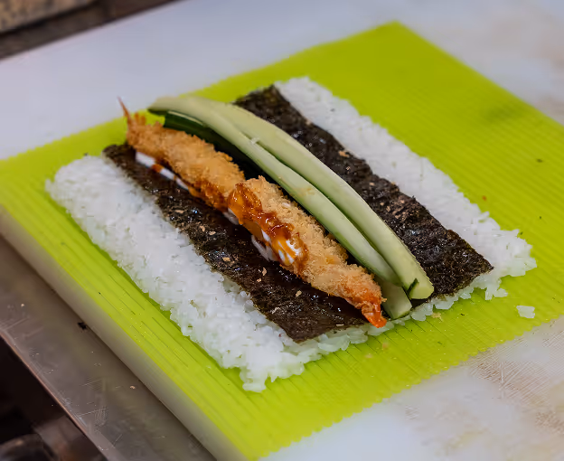 Sushi roll with shrimp, cucumber, and sauce on seaweed and rice.